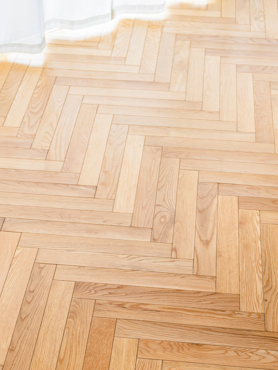 Parquet en bois clair, posé en chevrons, orienté vers le coin supérieur droit.