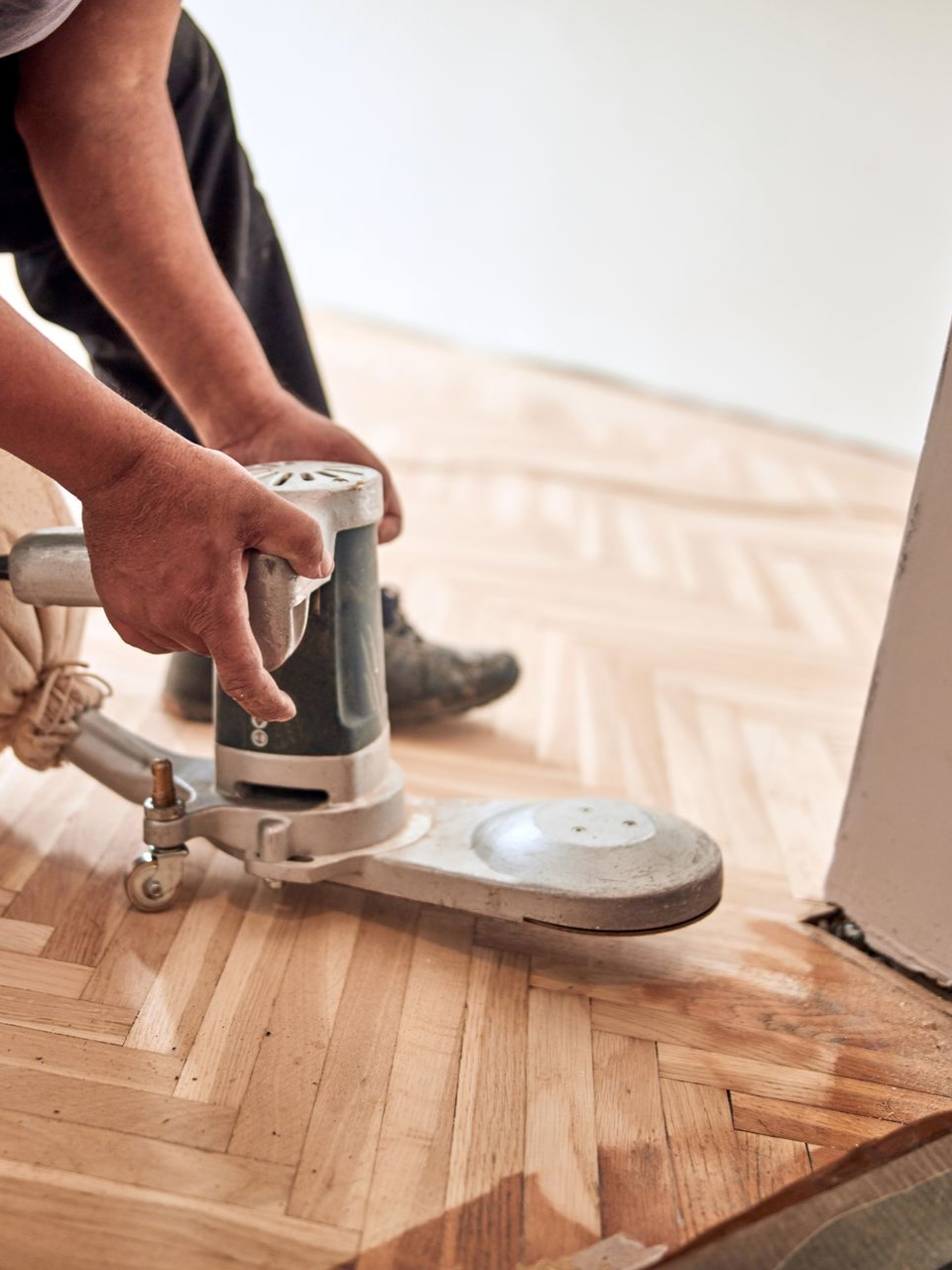 Personne ponçant un parquet avec une ponceuse électrique ; sciure de bois visible.