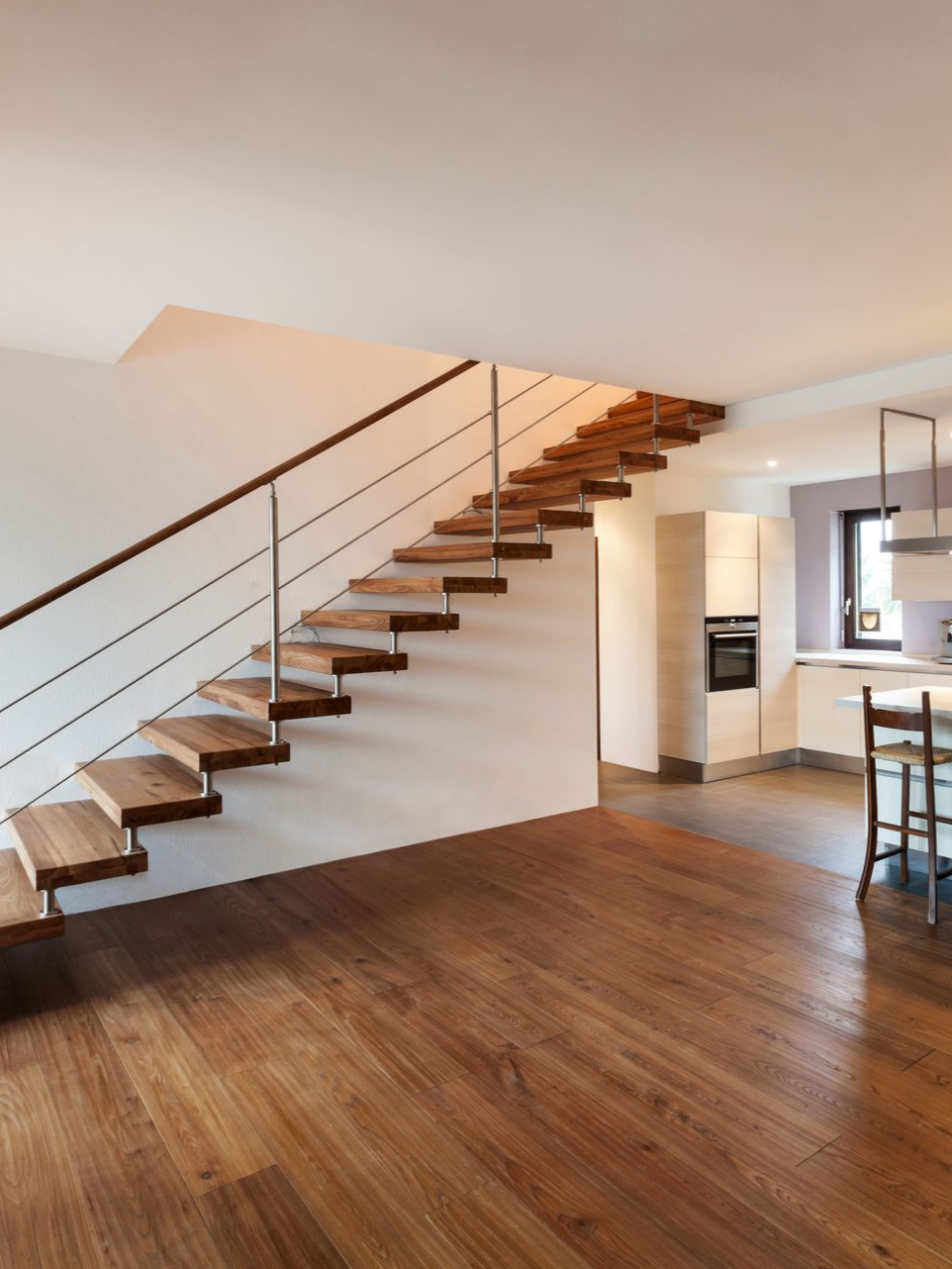 Escalier en bois avec rampe en métal dans un intérieur moderne, menant à une cuisine aux placards blancs.