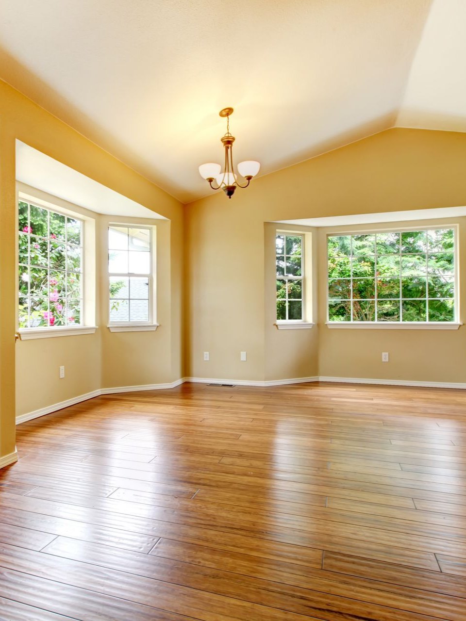 Pièce vide avec parquet, bow-window et lustre.