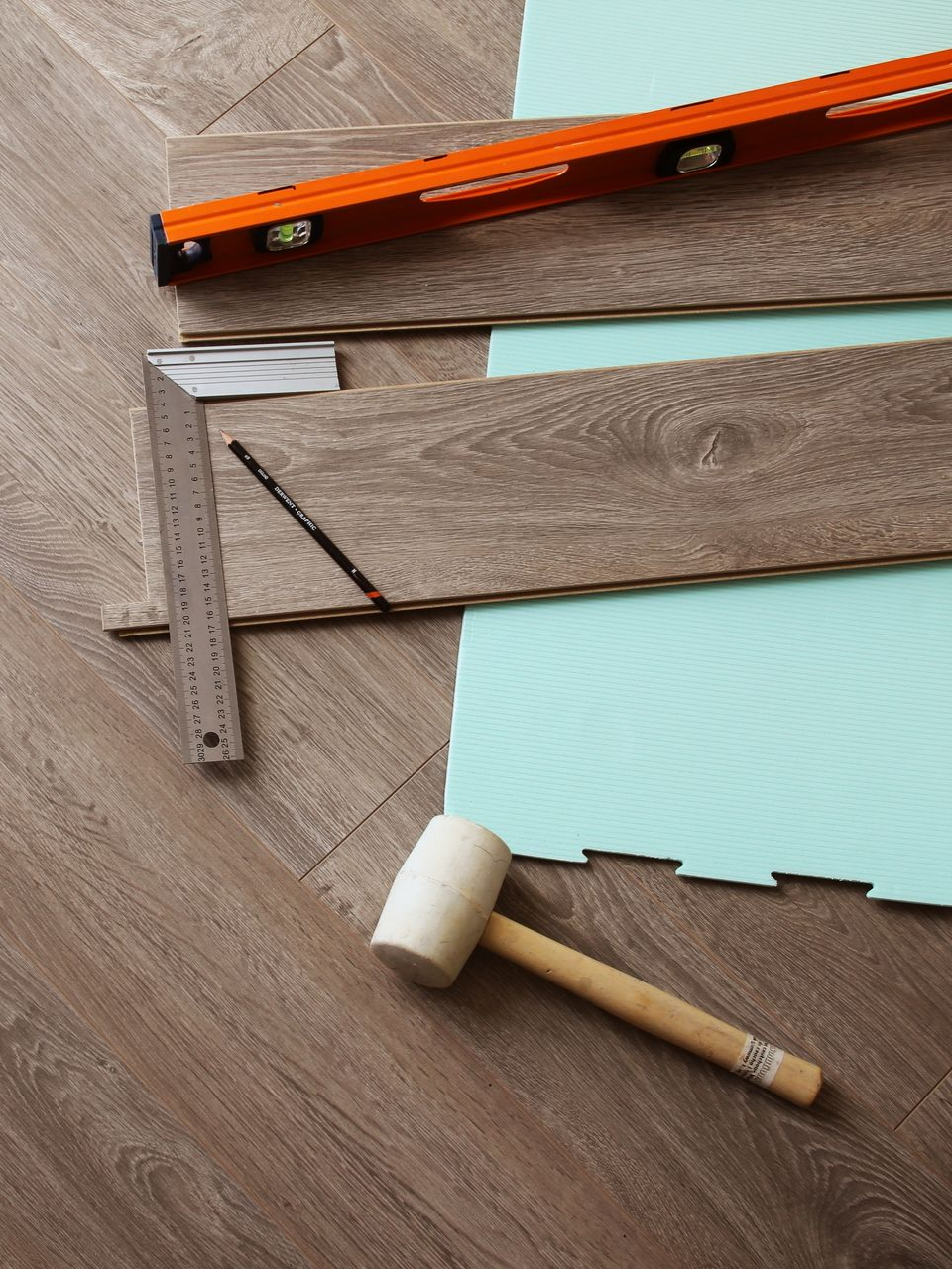 Pose du revêtement de sol avec outils : niveau, équerre, maillet et lames sur sous-couche.