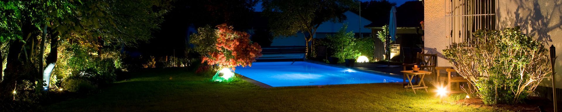 In einem Hinterhof ist ein großer Swimmingpool nachts beleuchtet.