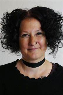 Eine Frau mit lockigem Haar trägt eine Halskette und lächelt.