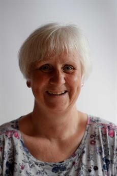 Eine Frau mit blondem Haar lächelt und trägt ein geblümtes Hemd.