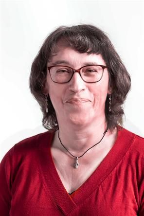Eine Frau mit Brille und rotem Pullover lächelt in die Kamera.