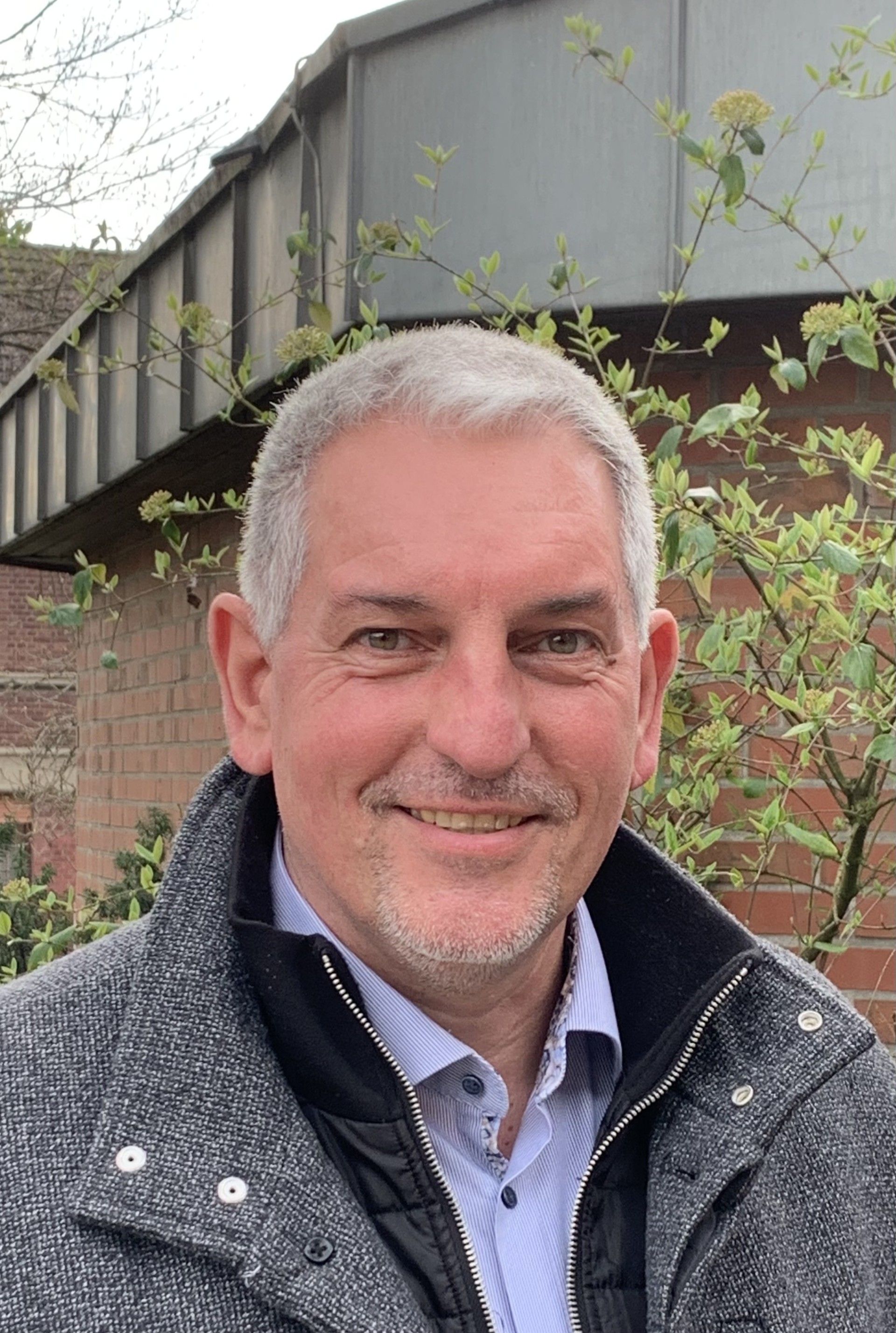 Ein Mann mit Bart lächelt und trägt ein weißes Hemd.