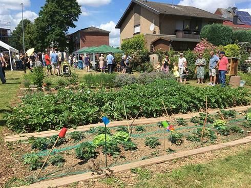 Eine Gruppe von Menschen steht in einem Garten, im Hintergrund ist ein Haus zu sehen.