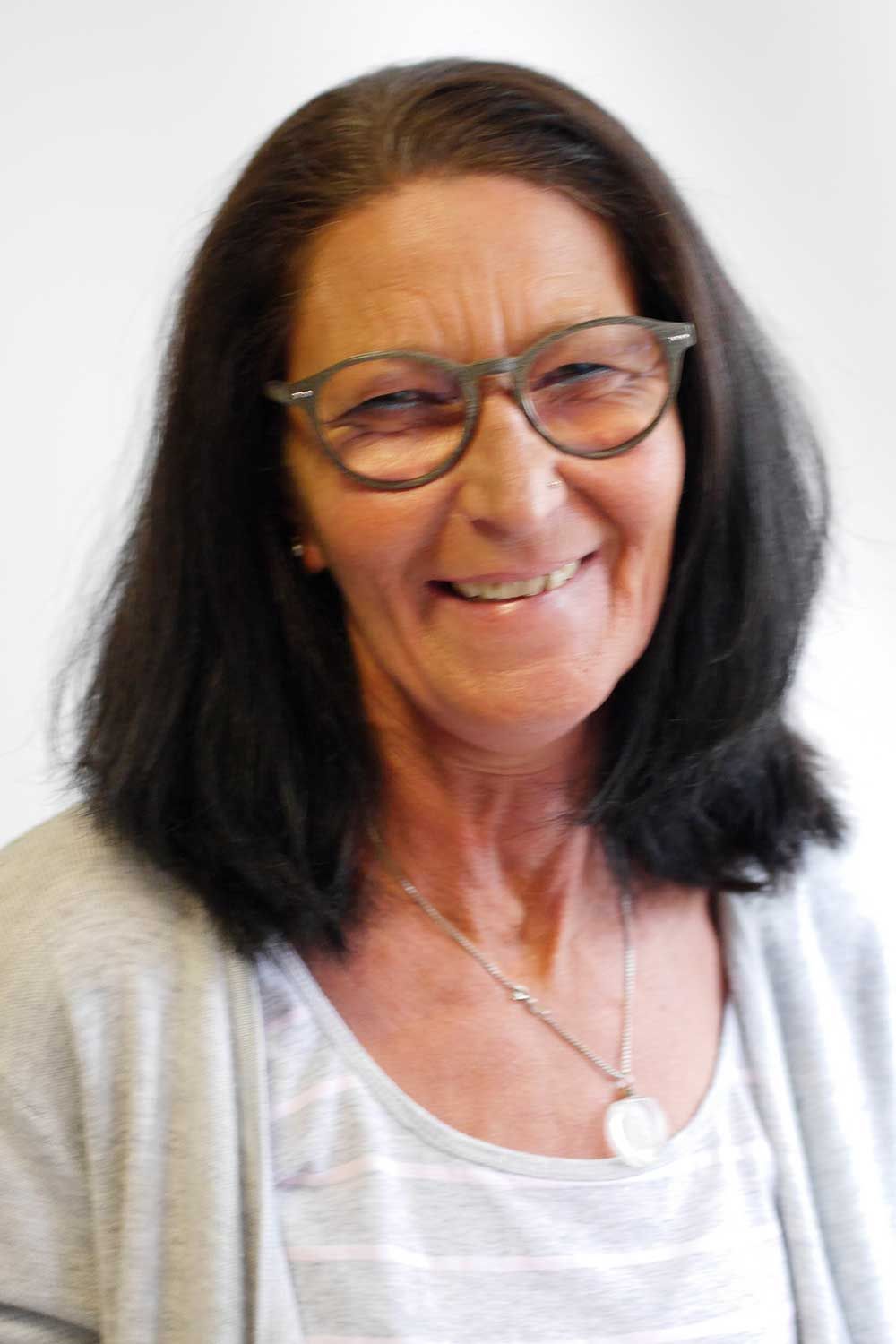 Eine Frau mit Brille und Halskette lächelt in die Kamera.