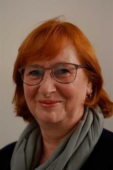 Eine Frau mit roten Haaren trägt eine Brille und ein Kopftuch.