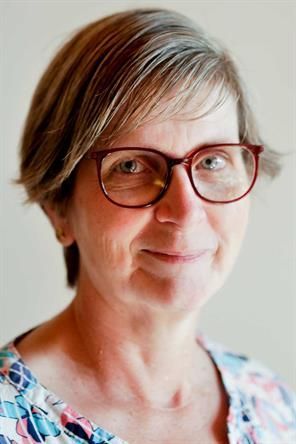 Eine Frau mit Brille und geblümtem Hemd lächelt in die Kamera.