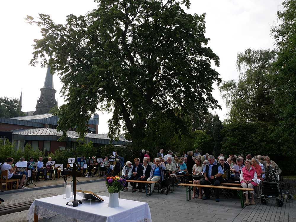 Eine Gruppe von Menschen sitzt unter einem Baum vor einer Kirche.