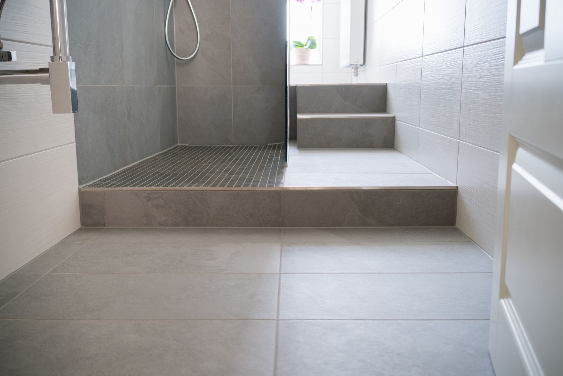 Douche moderne avec carrelage gris, tablette surélevée et murs carrelés blancs.
