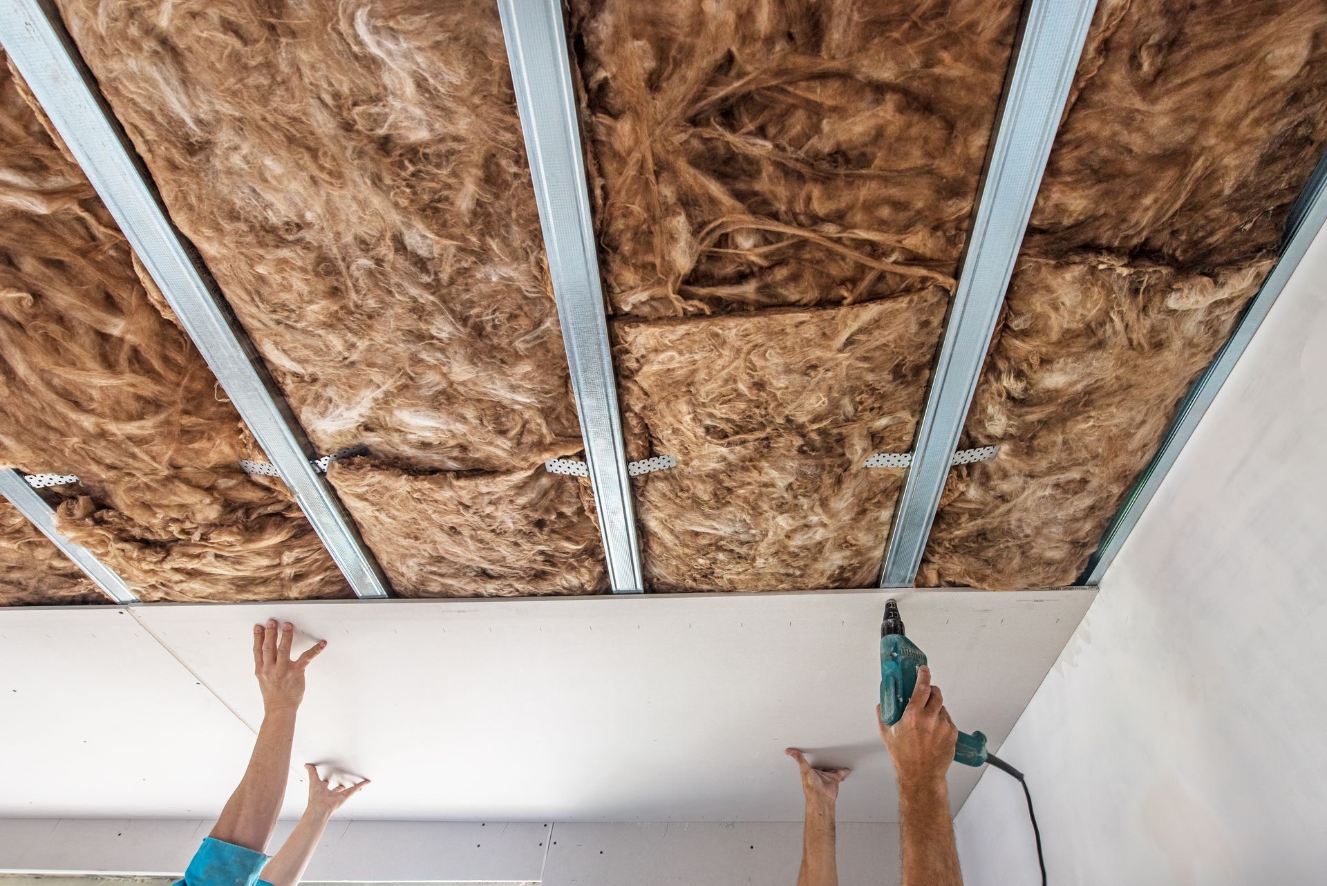 Deux ouvriers installent des panneaux d'isolation de plafond avec de la mousse expansive dans une pièce non finie