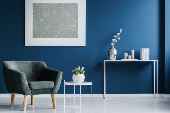 Salon bleu moderne avec un fauteuil gris, une table d'appoint, des tableaux et une console décorative