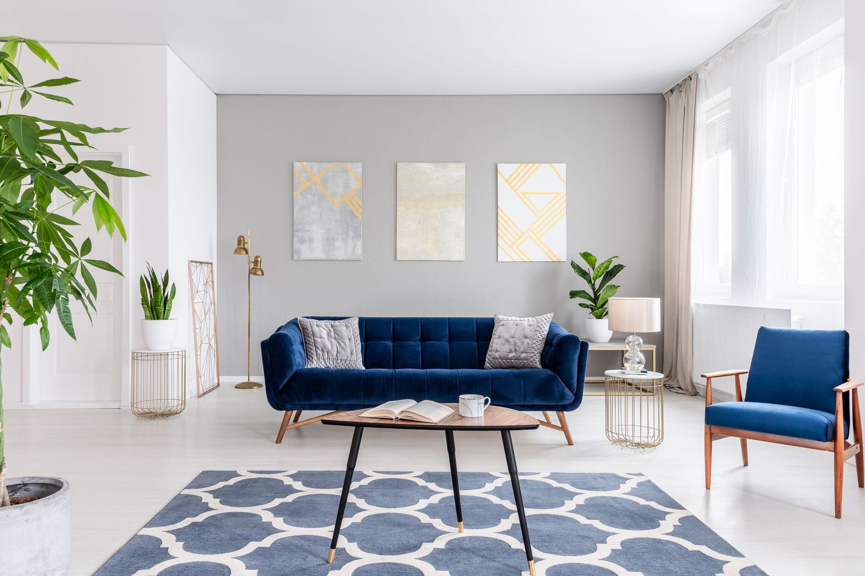Salon lumineux avec un canapé bleu marine, un fauteuil bleu, un tapis à motifs et de grandes fenêtres
