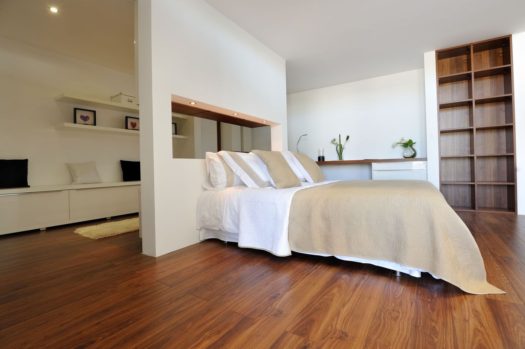 Chambre moderne et lumineuse avec parquet, lit blanc, étagères intégrées et vue dégagée sur la pièce adjacente