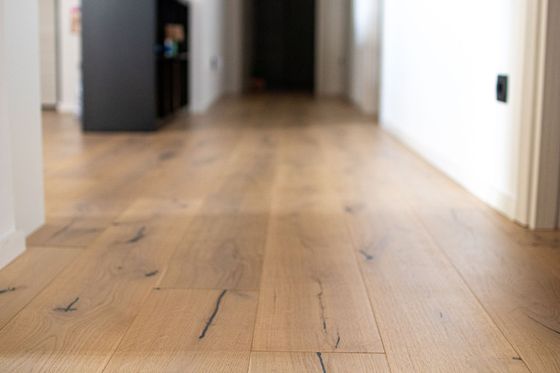 Couloir vide avec parquet clair et murs blancs donnant sur une porte.
