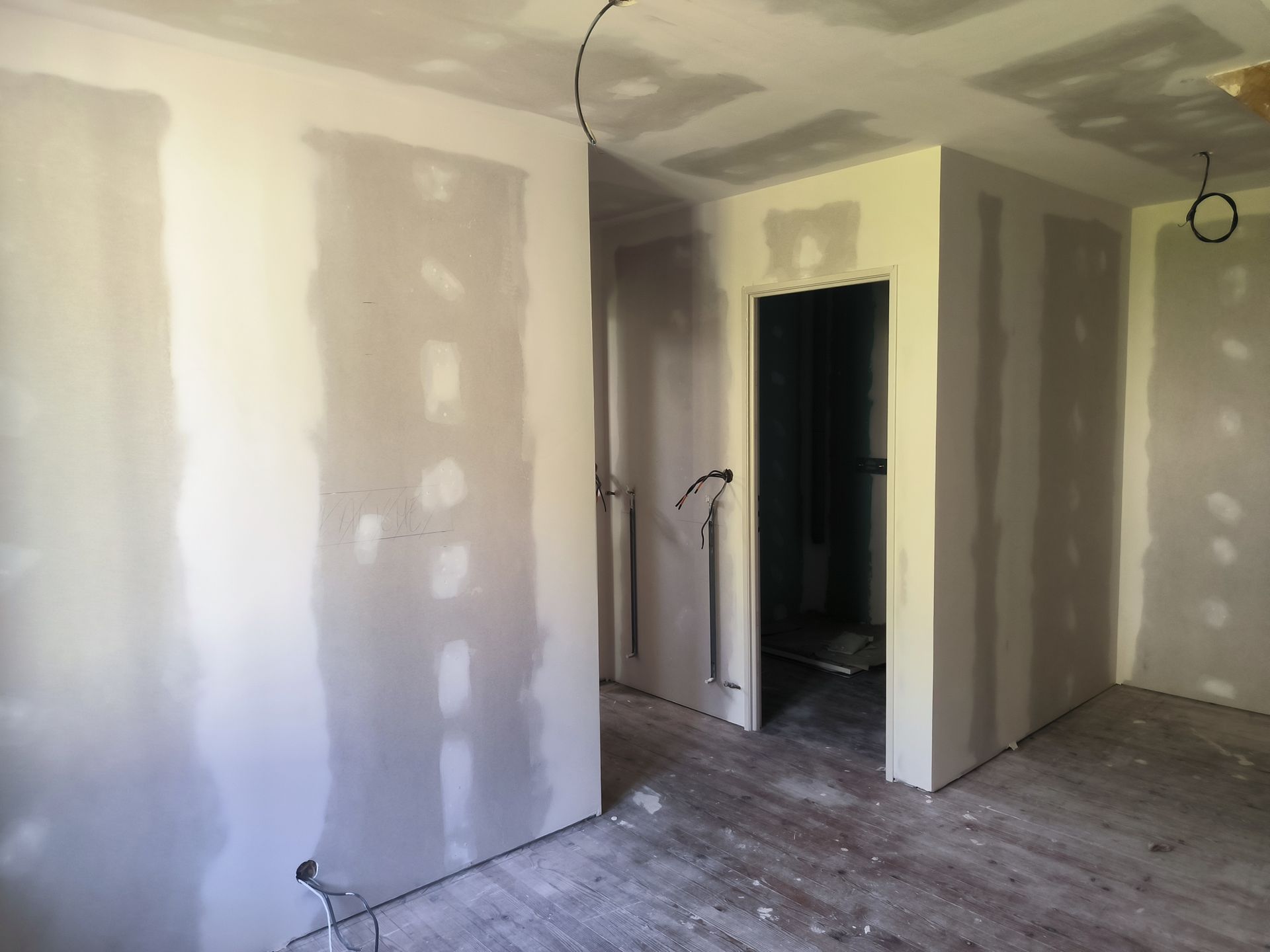 Intérieur en plaques de plâtre non finies avec joints collés, porte ouverte et sous-plancher nu.