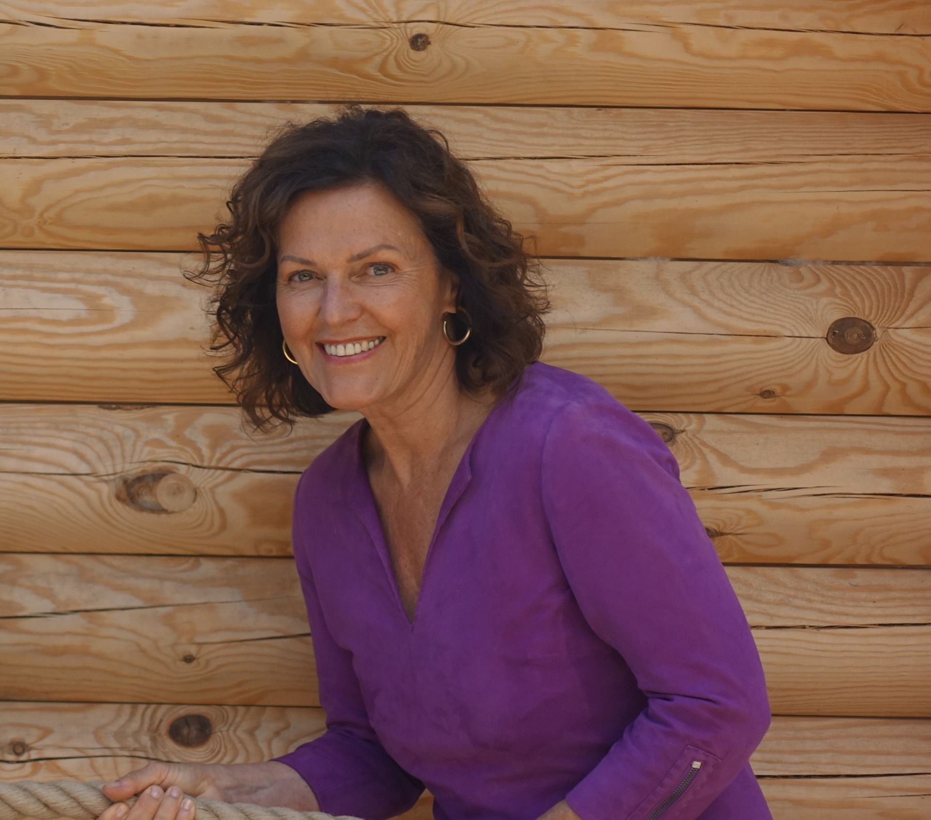 Eine Frau in einem lila Hemd lächelt vor einer Holzwand