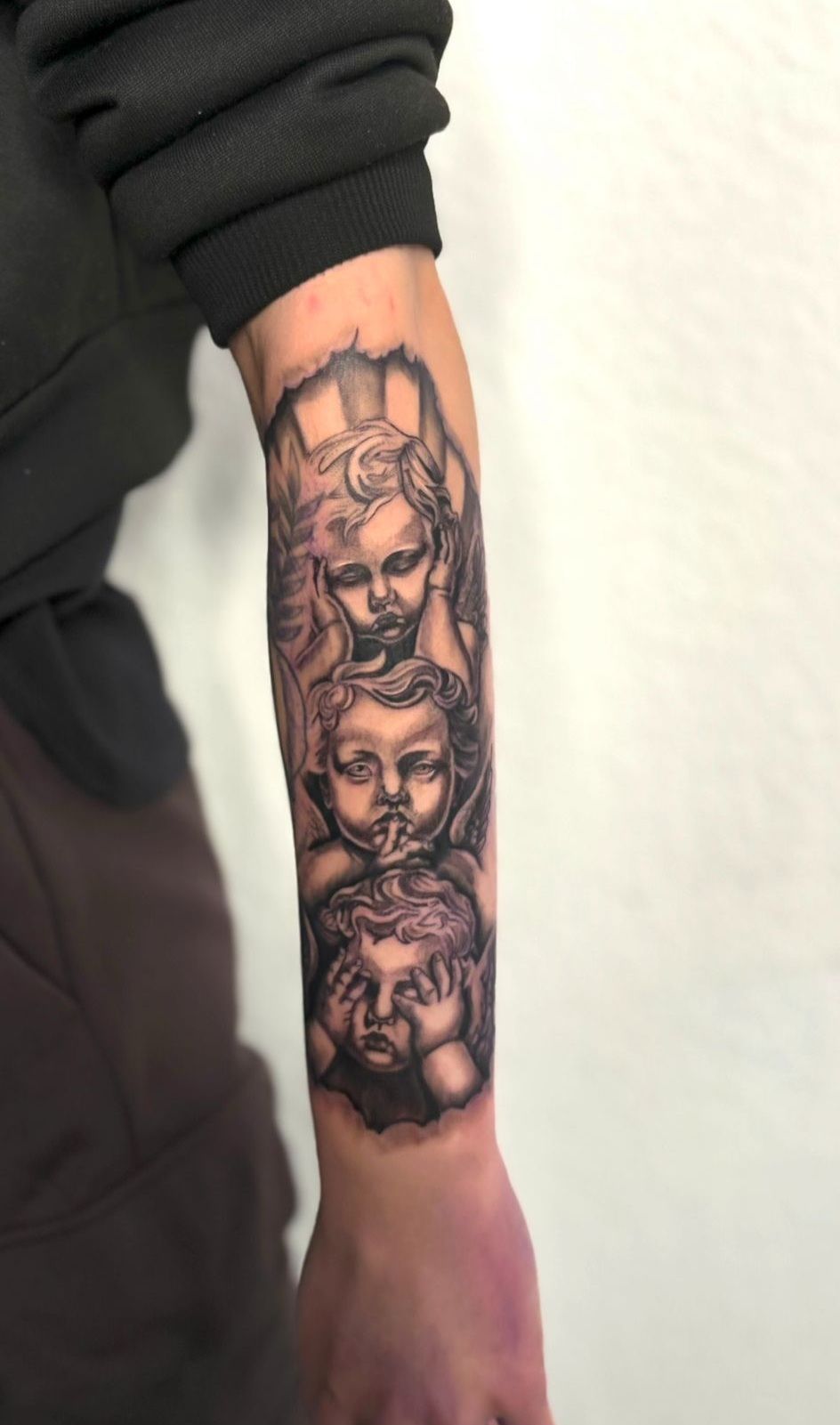 Eine Person hat eine Tätowierung von drei Engeln auf ihrem Unterarm.