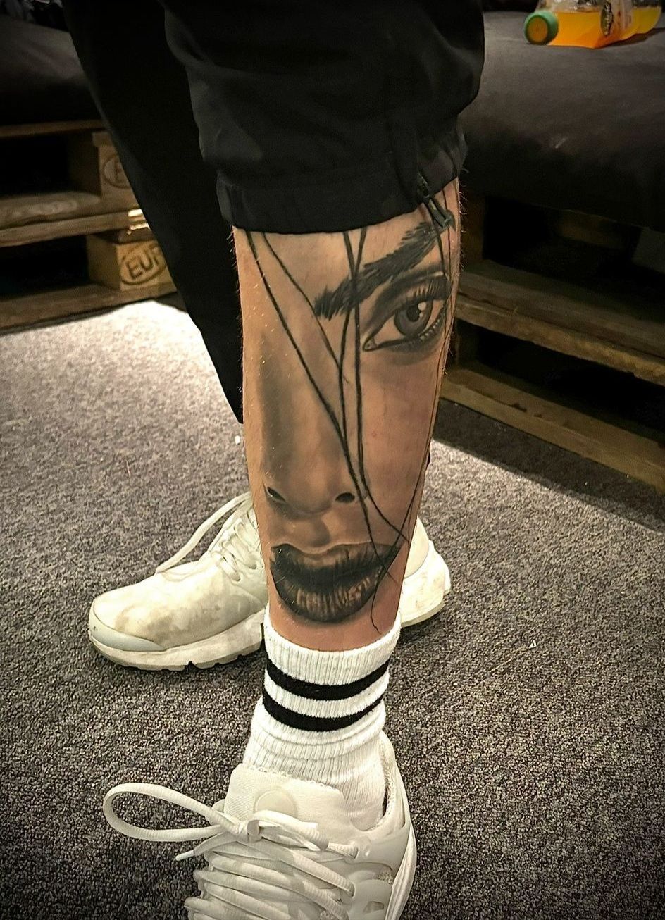 Eine Person mit einer Tätowierung eines Frauengesichts auf dem Bein.