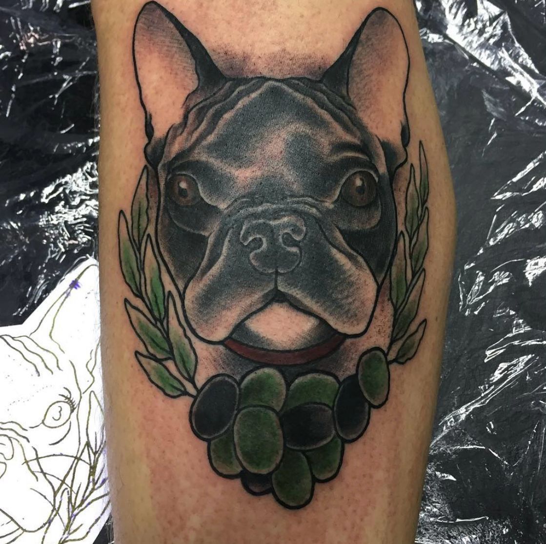 Ein Tattoo einer französischen Bulldogge mit einem Lorbeerkranz um den Hals