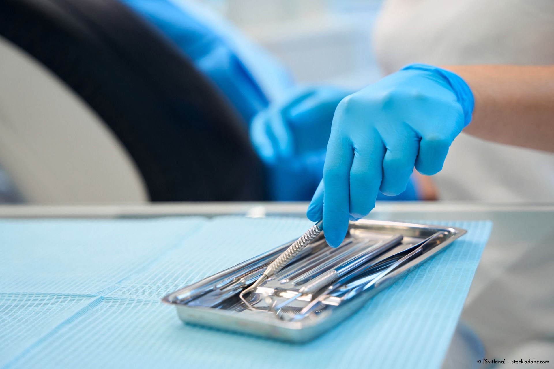 In klinischer Umgebung wählt behandschuhte Hand zahnärztliches Instrument vom Tablett.