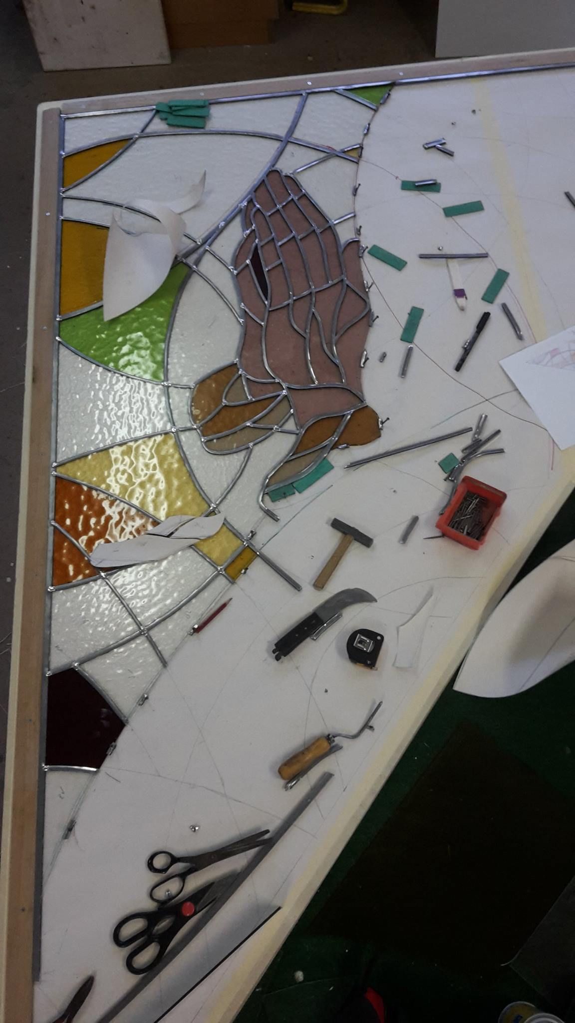 Auf einem Tisch mit Werkzeug wird ein Buntglasfenster gebaut.
