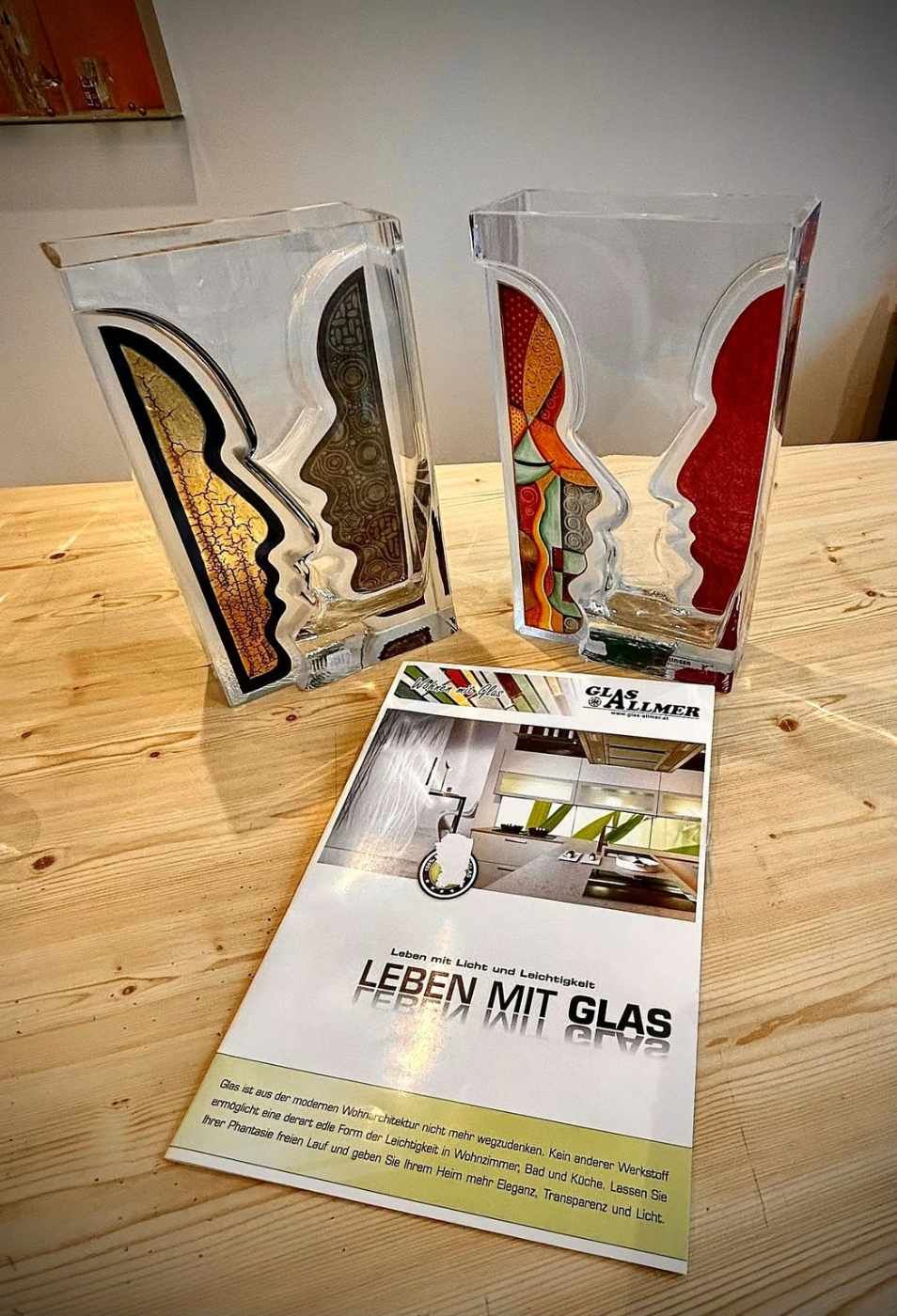 Zwei Vasen stehen neben einer Broschüre auf einem Holztisch.