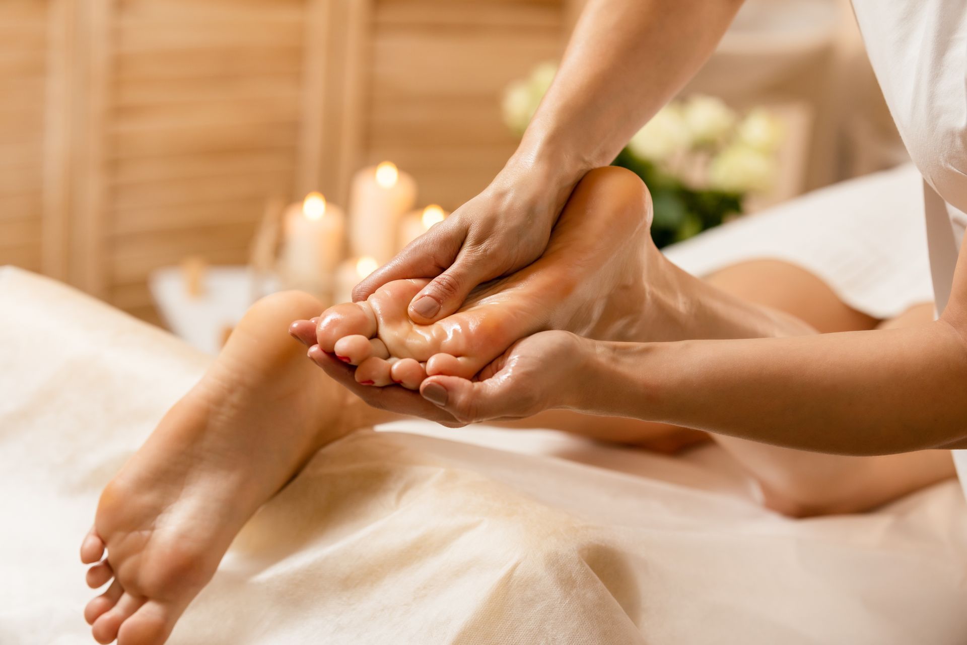 Fussmassage mit Öl, Nahaufnahme. Der Fuss einer Person wird auf einem weissen Handtuch massiert, im Hintergrund Kerzen.