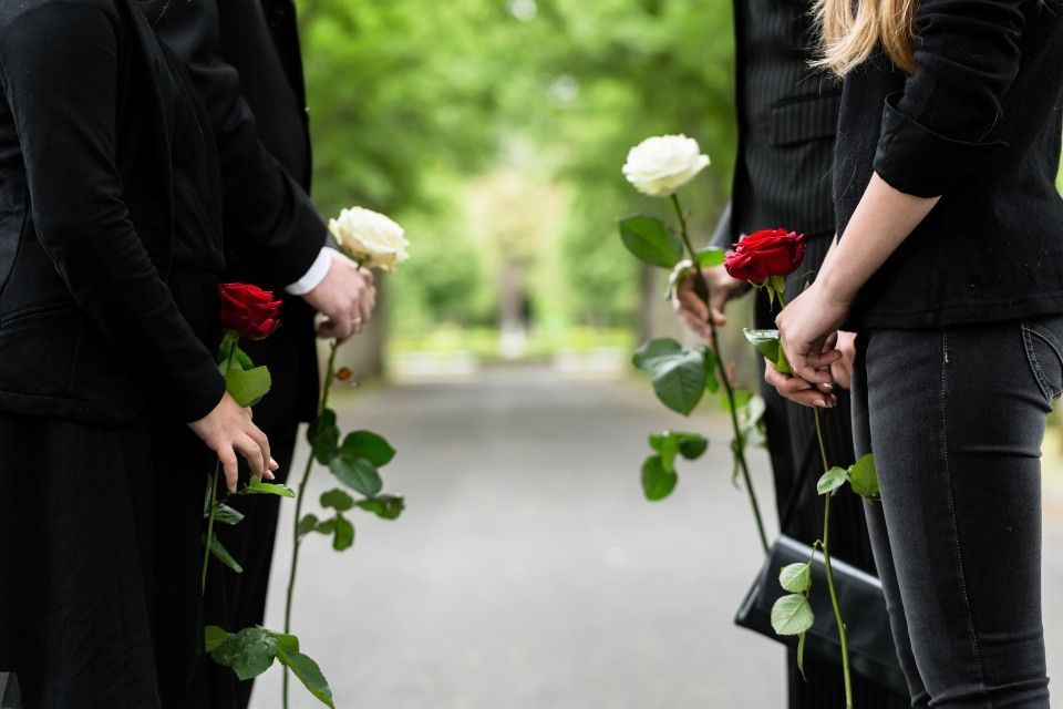 Rolf Knoben Beerdigungsinstitut - Hinterbliebene mit Blumen an einem Grabmal