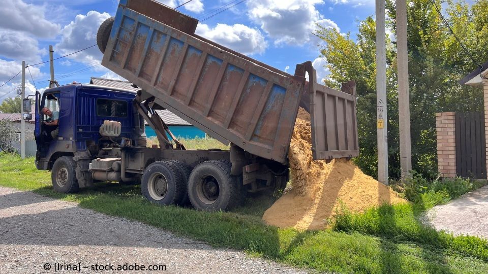Ein Muldenkipper kippt Erde am Straßenrand ab. Sattler Bau- und Handels GmbH