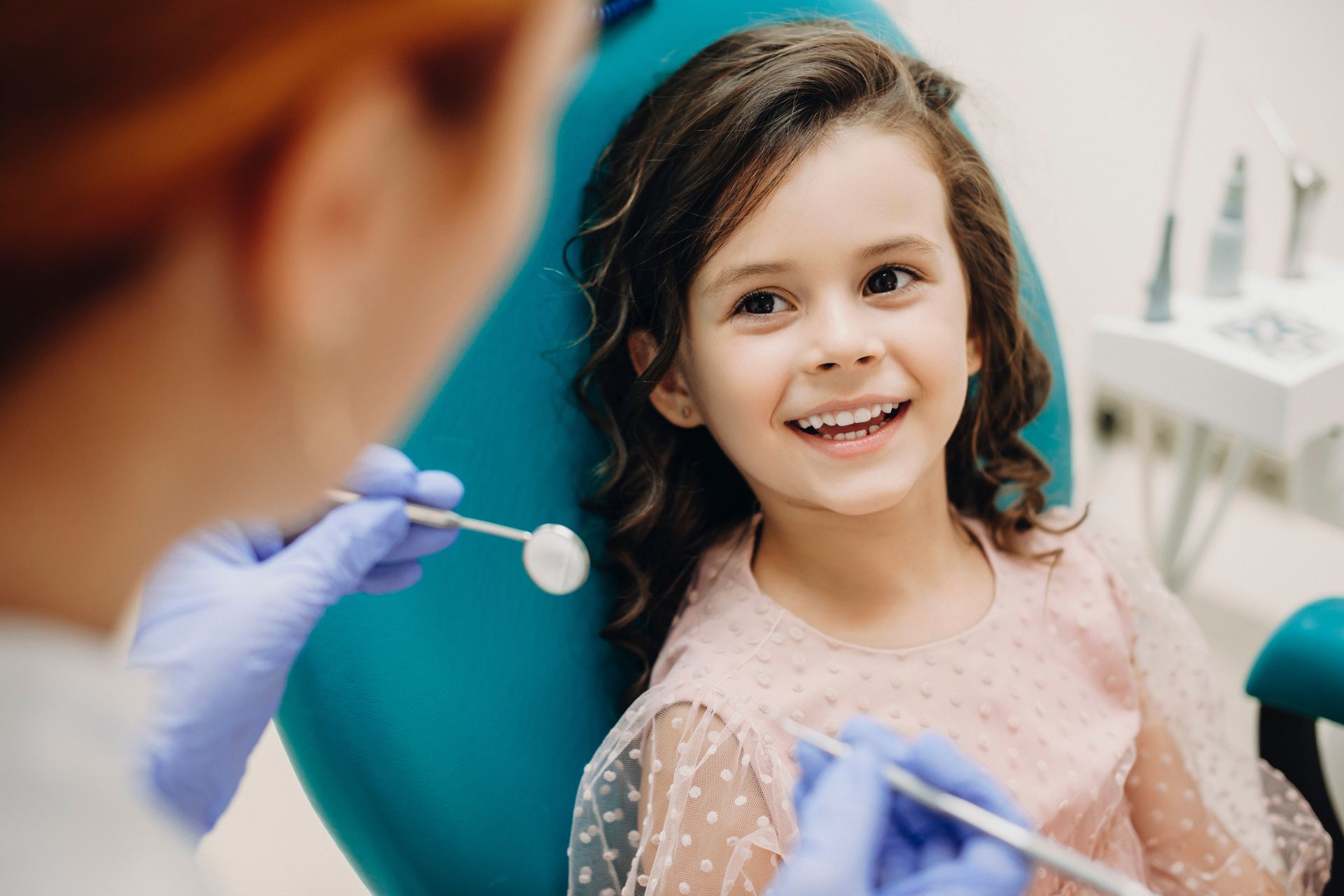 Una bambina è seduta sulla poltrona del dentista mentre un dentista le esamina i denti.
