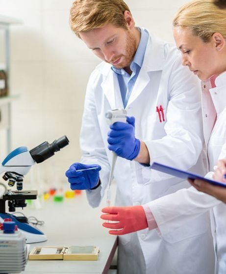 Un hombre y una mujer están trabajando en un laboratorio con un microscopio y un portapapeles.