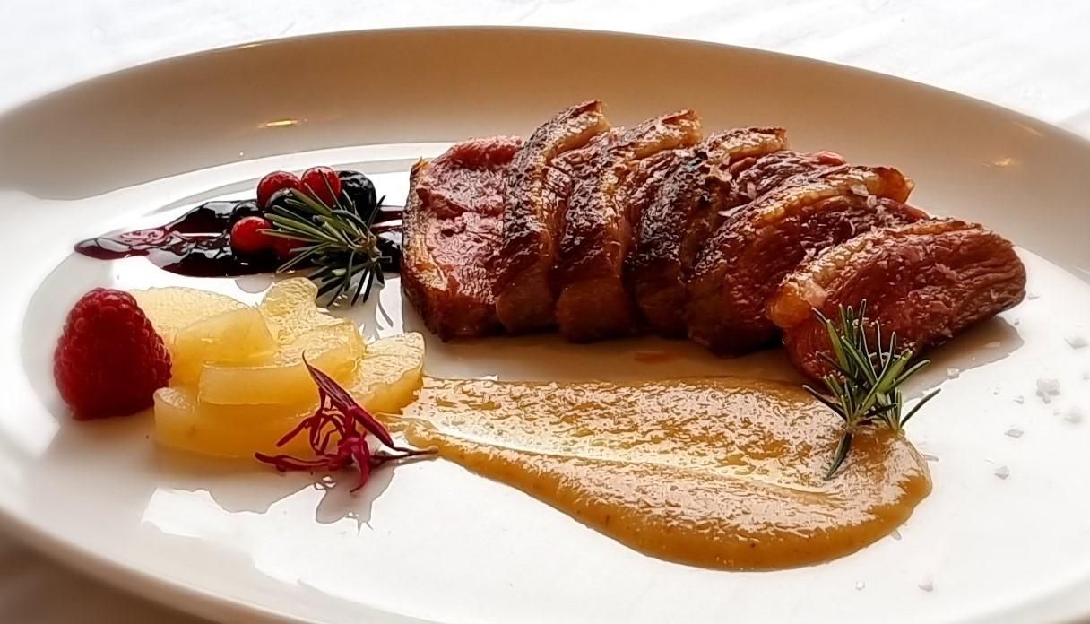 Pechuga de pato en rodajas con salsa, bayas y manzanas en un plato blanco.