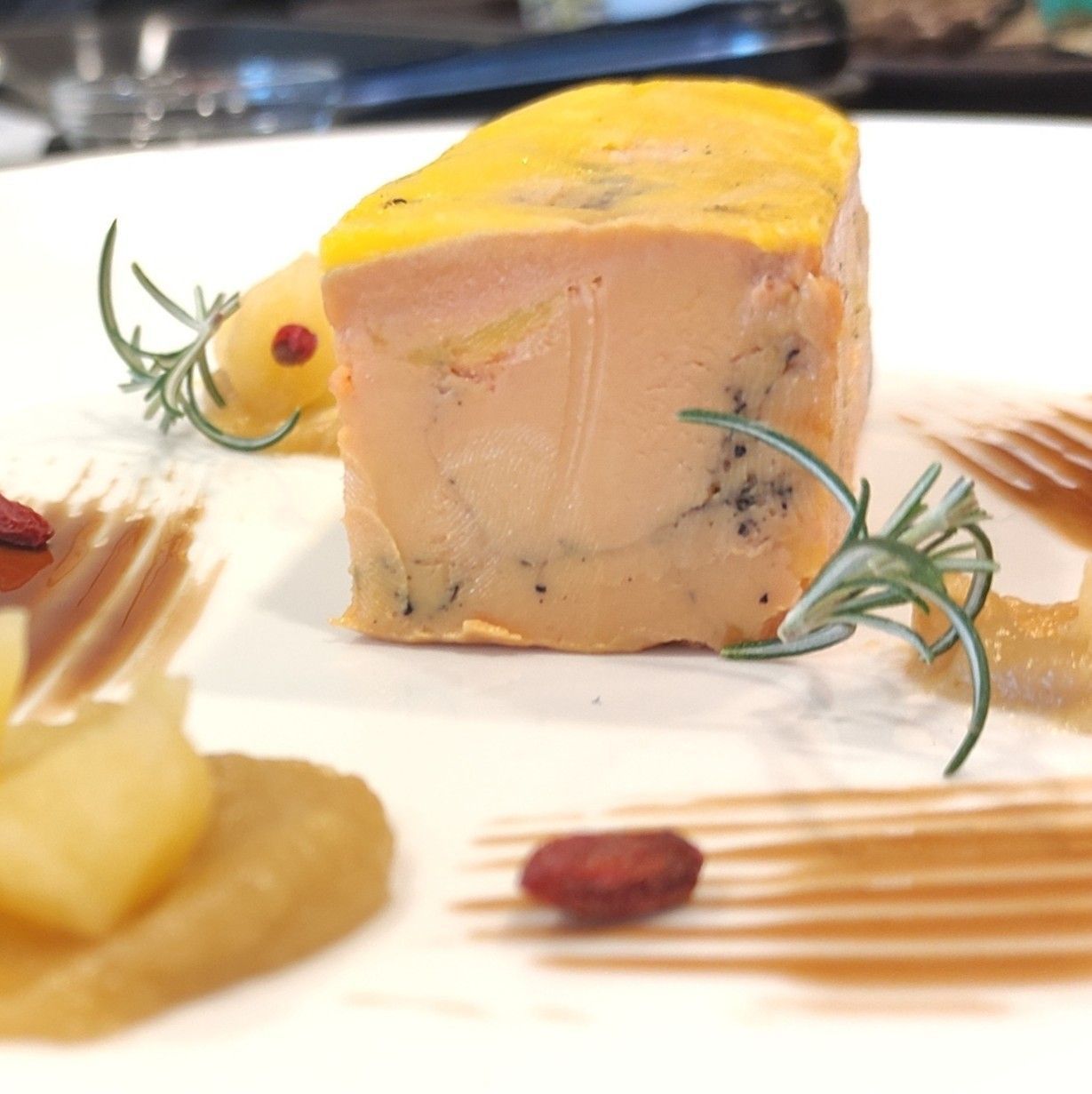 Foie gras con glaseado amarillo, romero y fruta en un plato blanco.