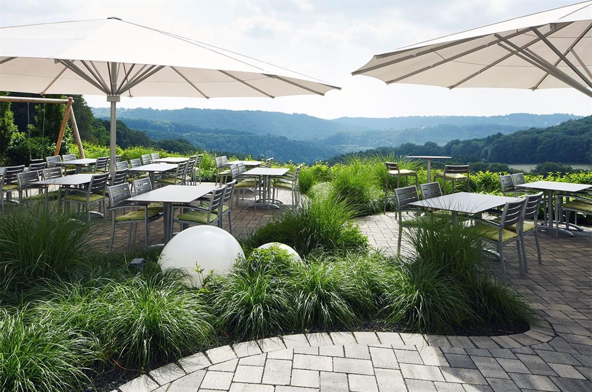 Eine Terrasse mit Tischen, Stühlen und Sonnenschirmen mit Blick auf ein Tal