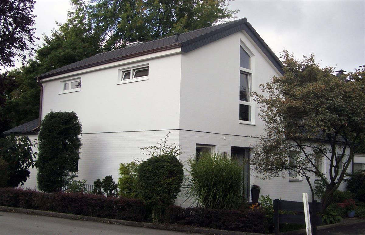 Ein weißes Haus mit schwarzem Dach ist von Büschen und Bäumen umgeben