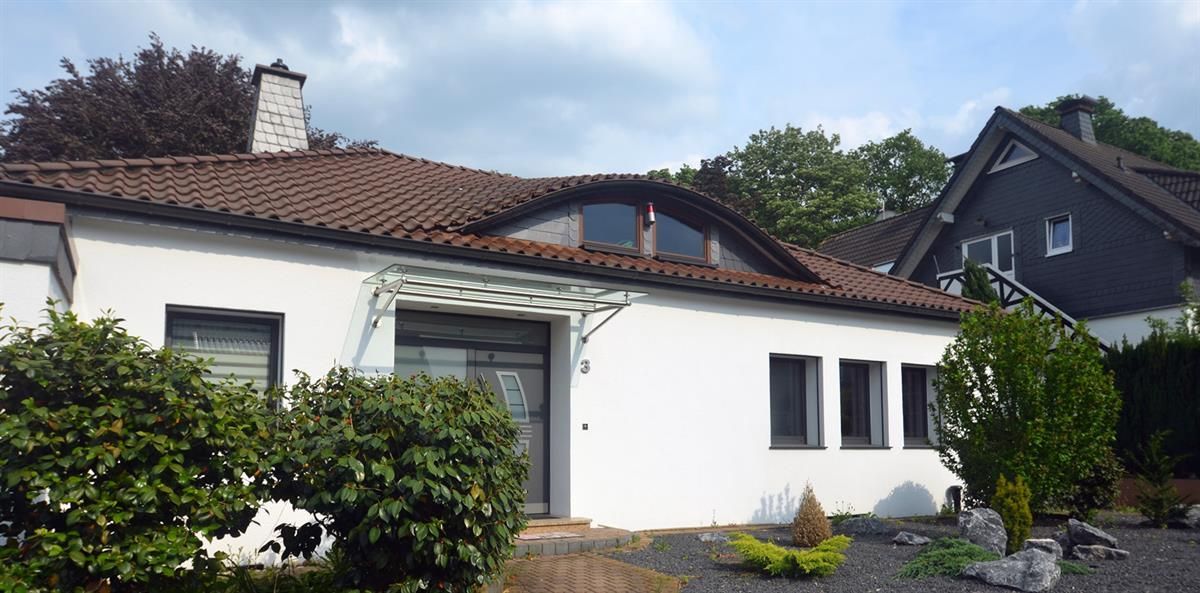 Ein weißes Haus mit einem braunen Dach ist von Büschen umgeben