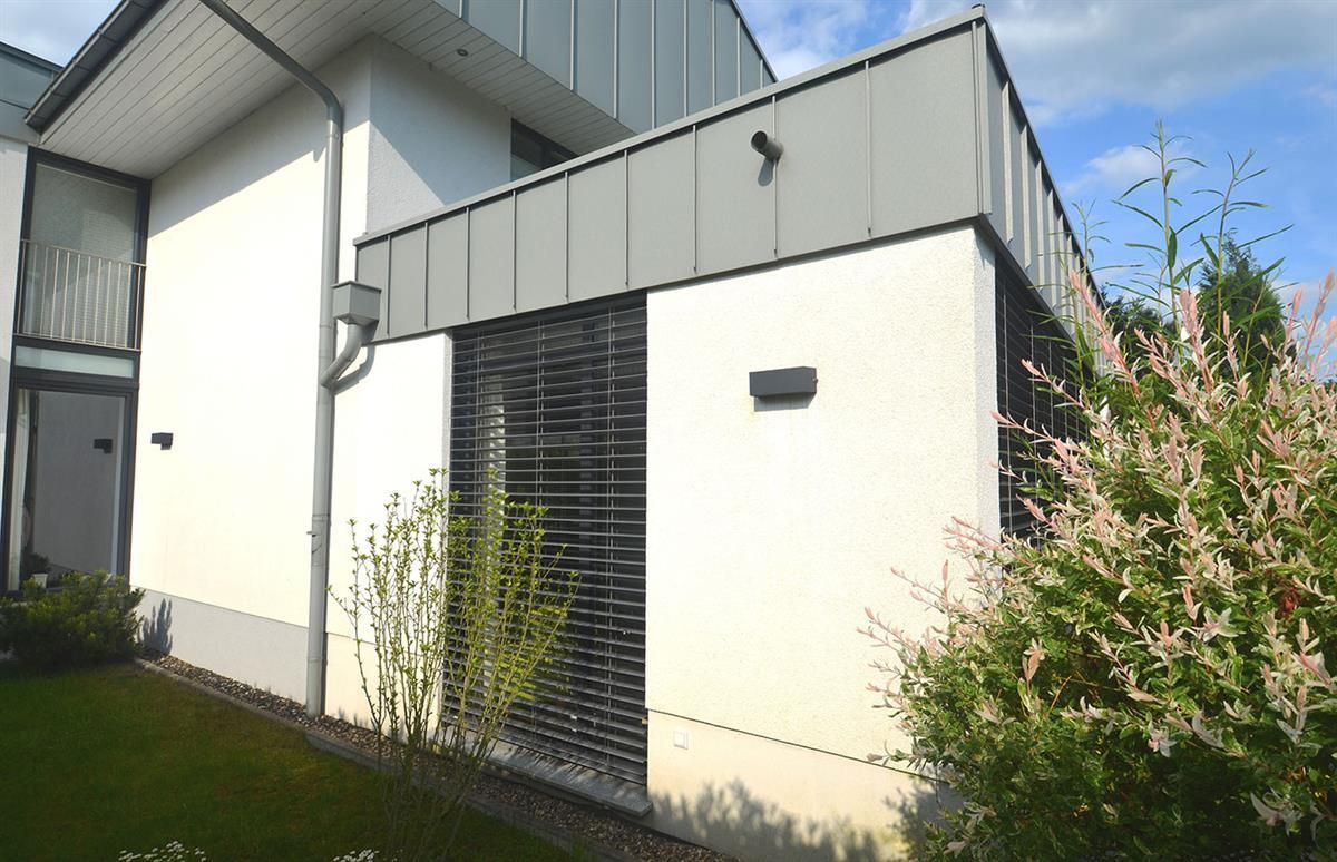 Ein weißes Haus mit grauem Dach und einem Busch davor