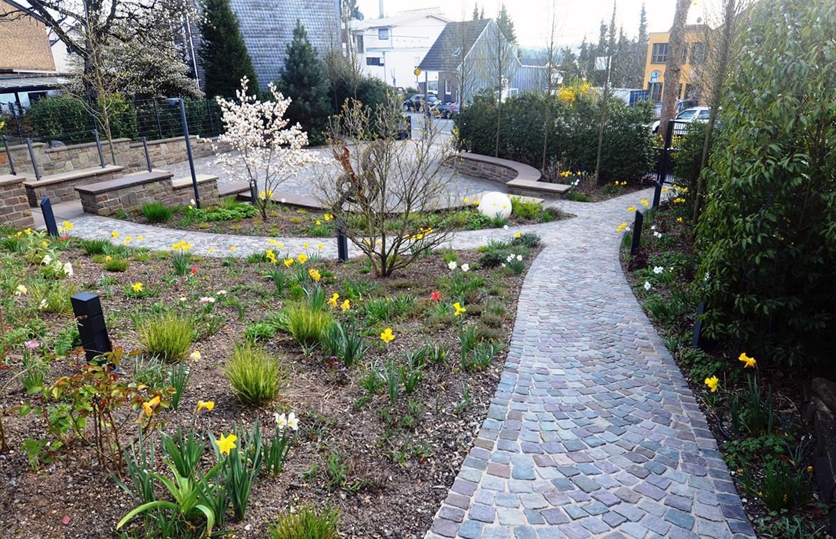 Ein gemauerter Gehweg in einem Garten mit Blumen und Bäumen