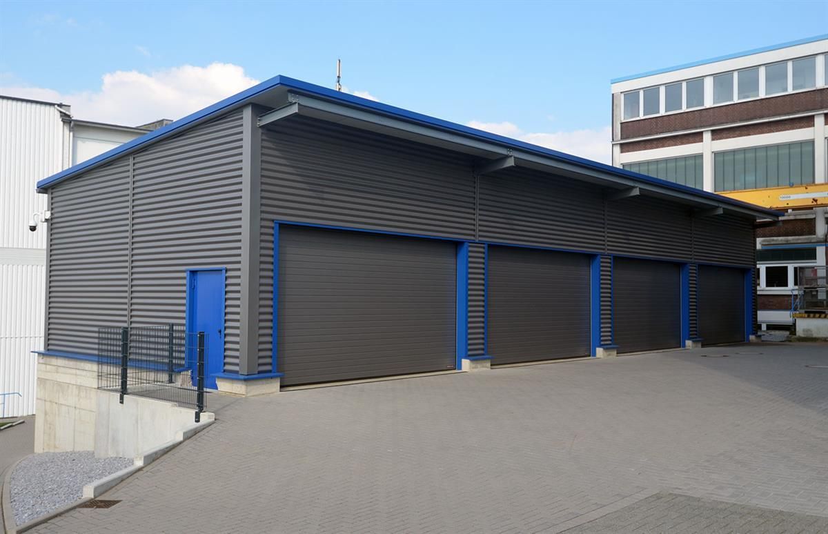 Ein Gebäude mit drei Garagentoren und einem Backsteingebäude im Hintergrund