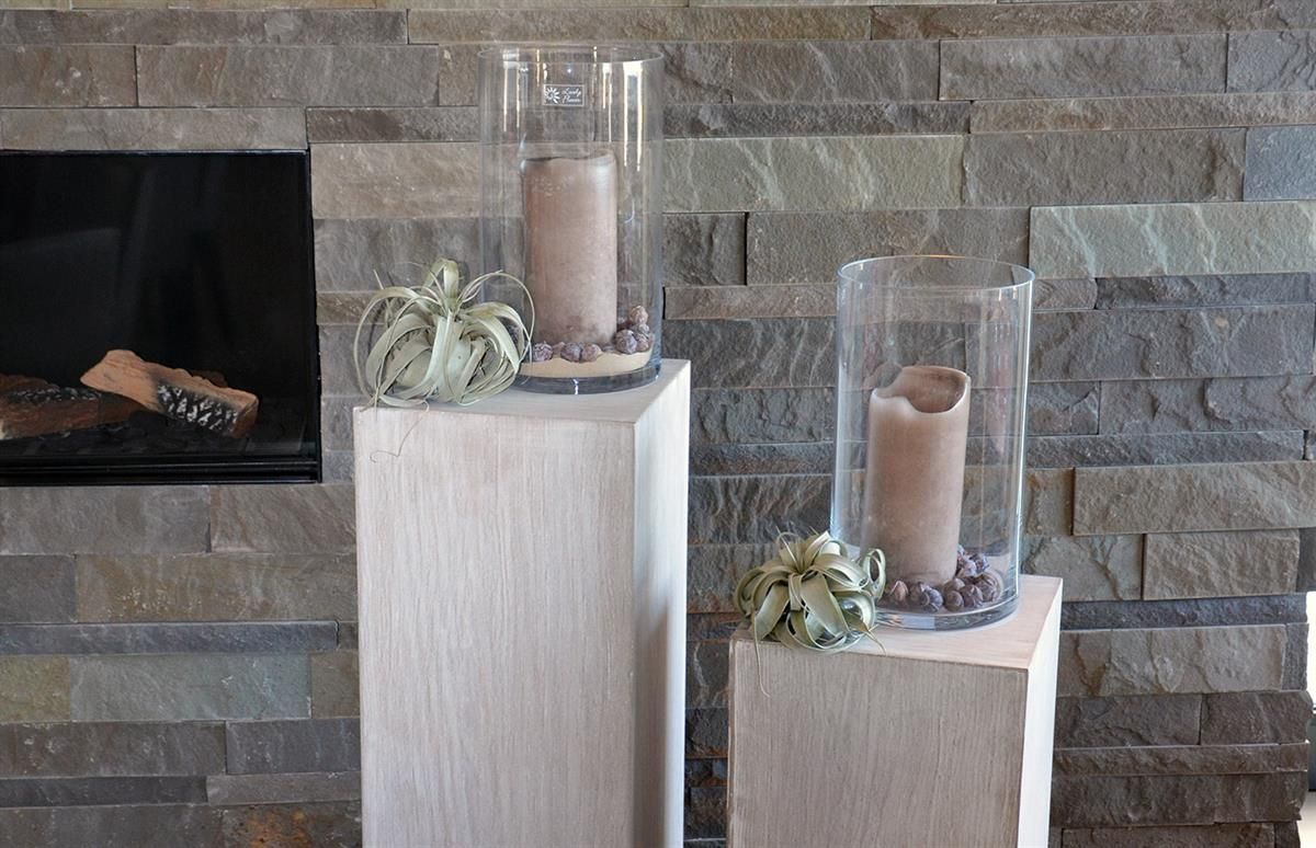 Zwei Kerzen stehen auf einem Holzsockel vor einem Kamin.