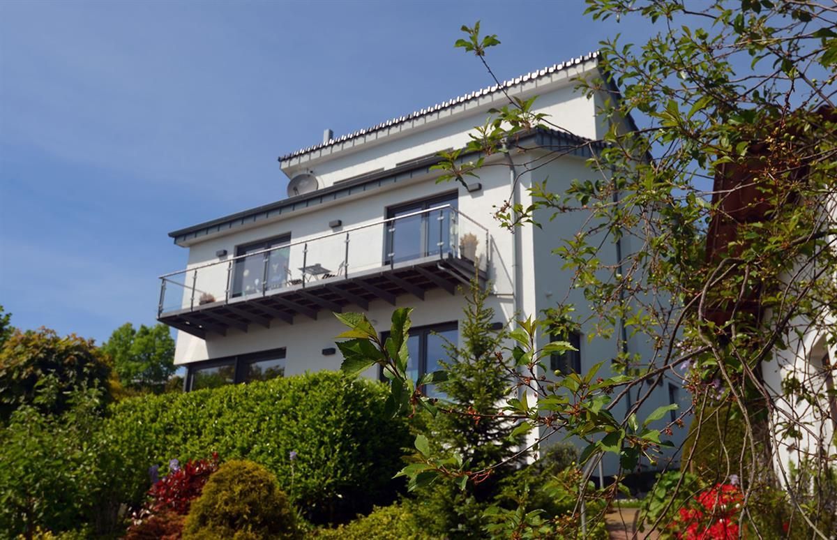 Ein weißes Haus mit Balkon ist von Bäumen und Sträuchern umgeben