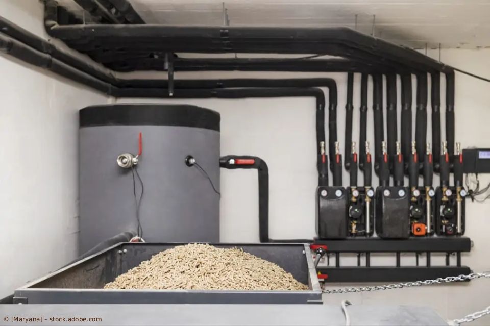 Eine Holzpellet-Heizkesselanlage im Keller mit großem Speichertank, Heizmaterialbehälter und isolierten Rohren.