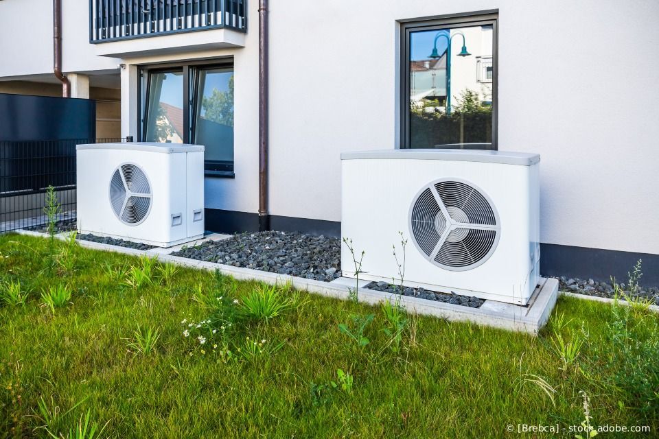 Zwei weiße Außenwärmepumpen wurden auf Betonfundamenten vor einem modernen Haus mit Rasenfläche installiert.