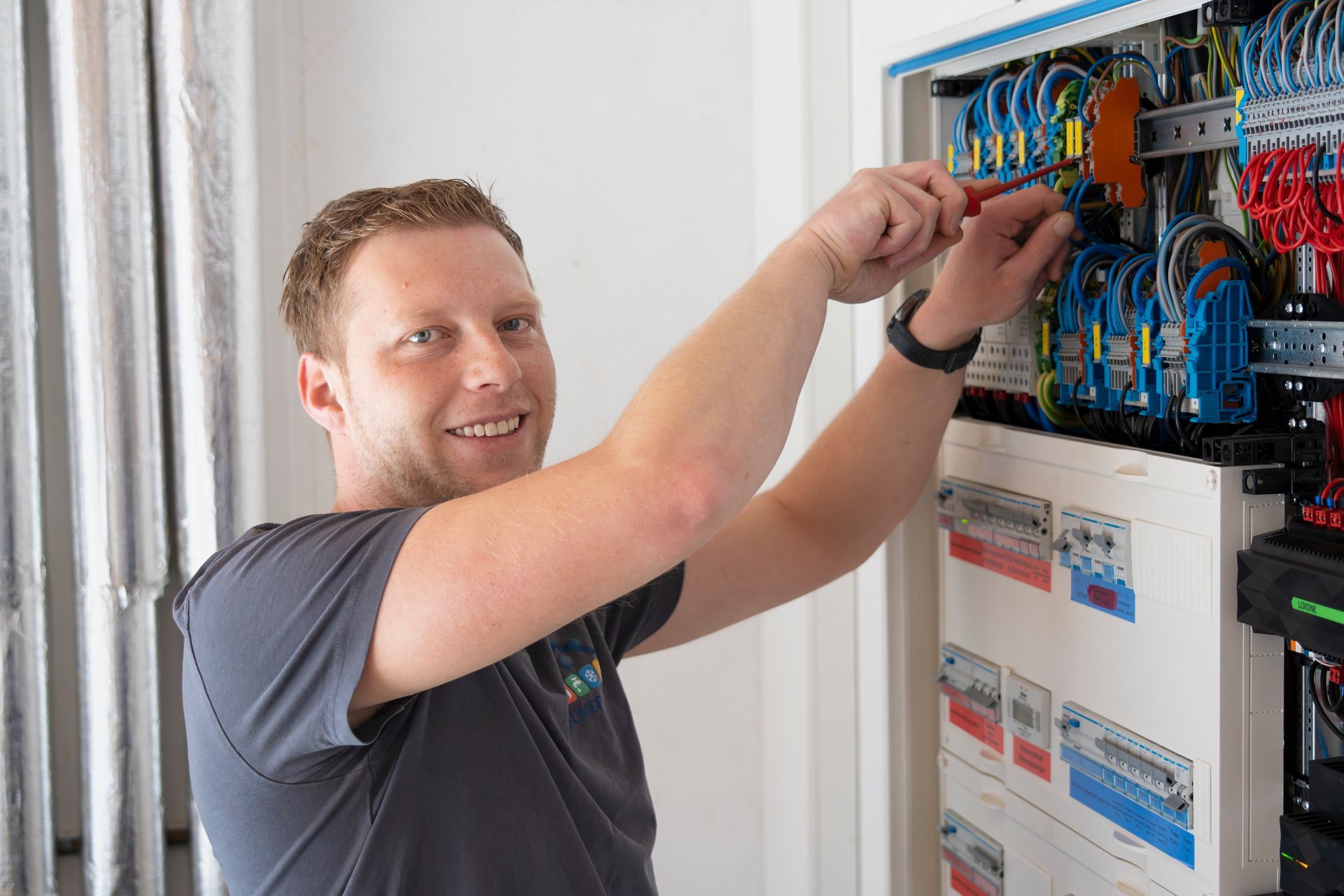 Nahaufnahme von Händen, die mit einem Schraubendreher eine Drahtverbindung an einem elektrischen Sicherungskasten festziehen.