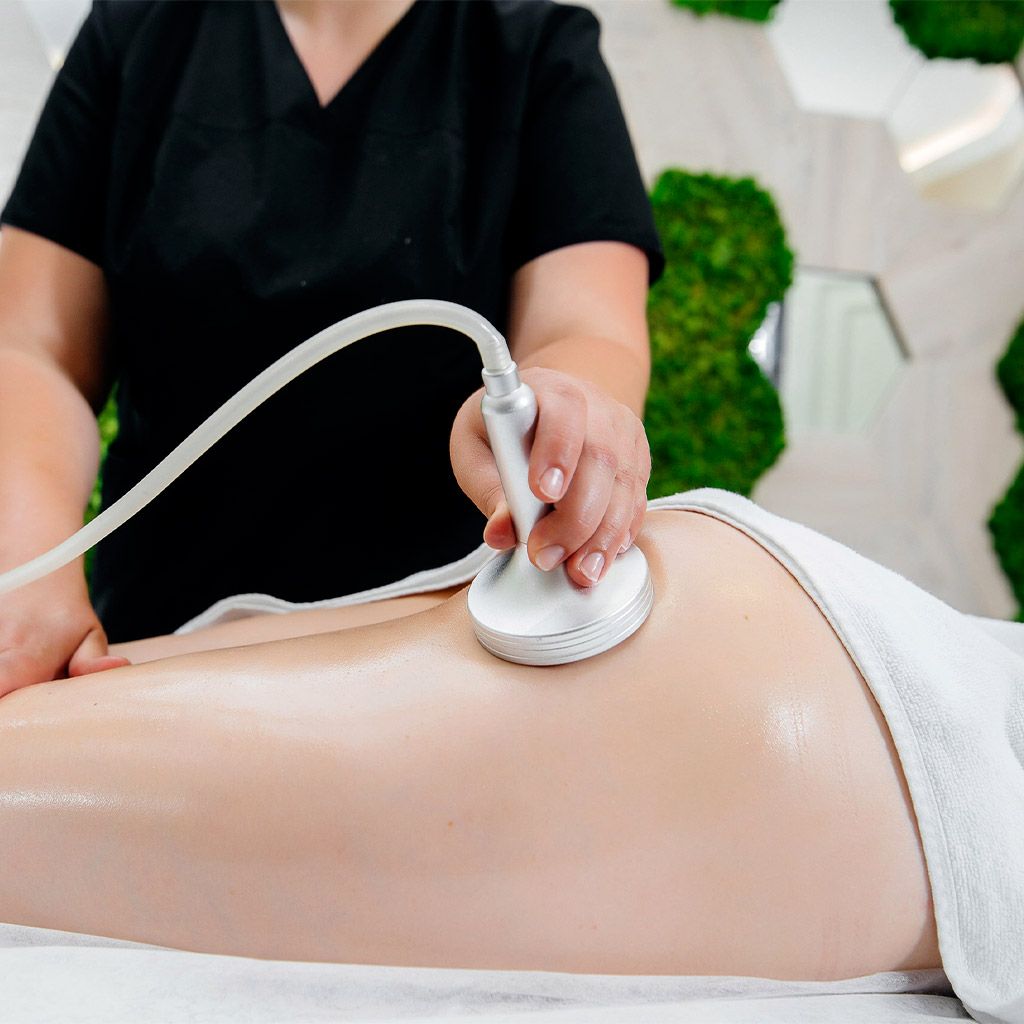 Esteticista utilizando un dispositivo de ultrasonido portátil en el abdomen desnudo de una clienta durante un tratamiento de spa.