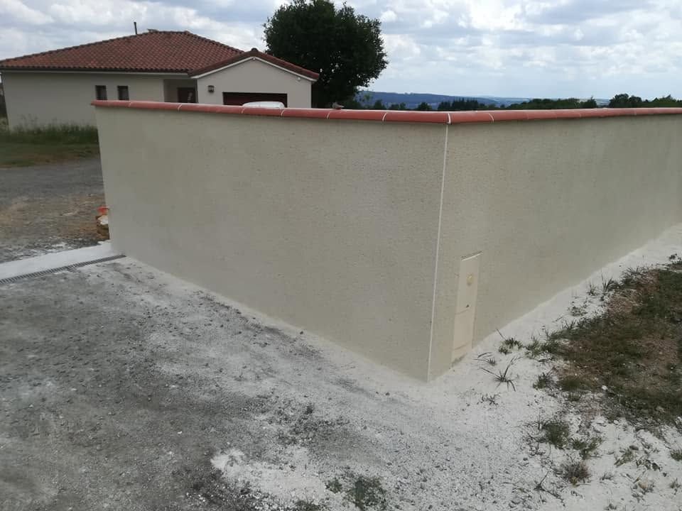Coin de mur beige bordant une allée de gravier, avec une maison en arrière-plan.