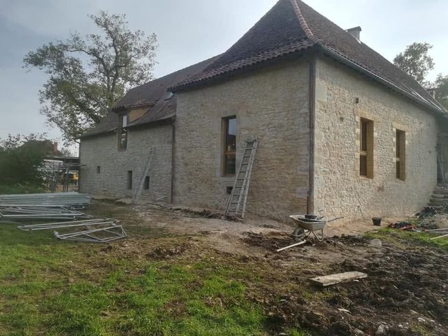 Maison en pierre en construction, toit de tuiles, échelle contre le mur et matériaux de construction dans la cour